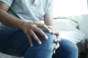 Man Suffering Knee Joint Pain Sitting On Bed